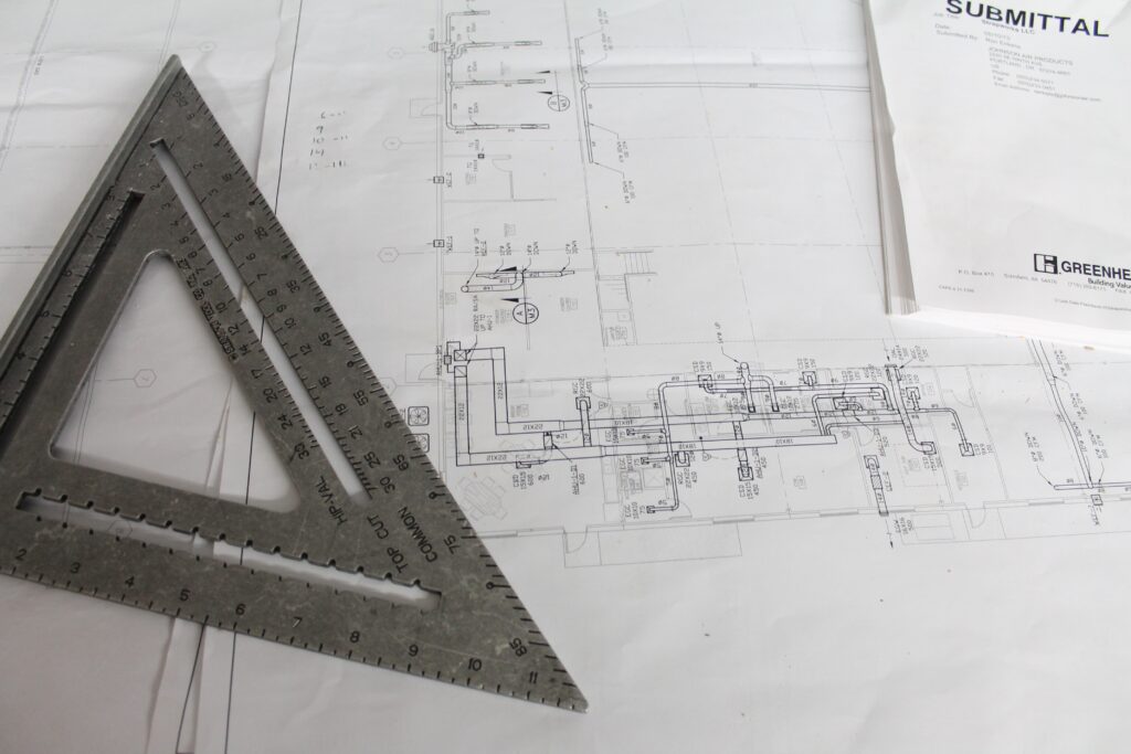 Régua e esquadro sobre planta técnica de arquitetura, representando a etapa de concepção do projeto